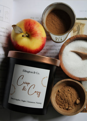 Candle labeled 'Ellington & Co. Crisp & Cozy' with an apple, sugar, and cinnamon on a newspaper background.