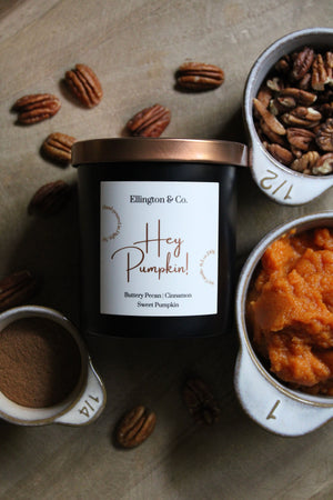 Candle labeled 'Hey Pumpkin!' by Ellington & Co. with pecans and pumpkin puree on a wooden surface.